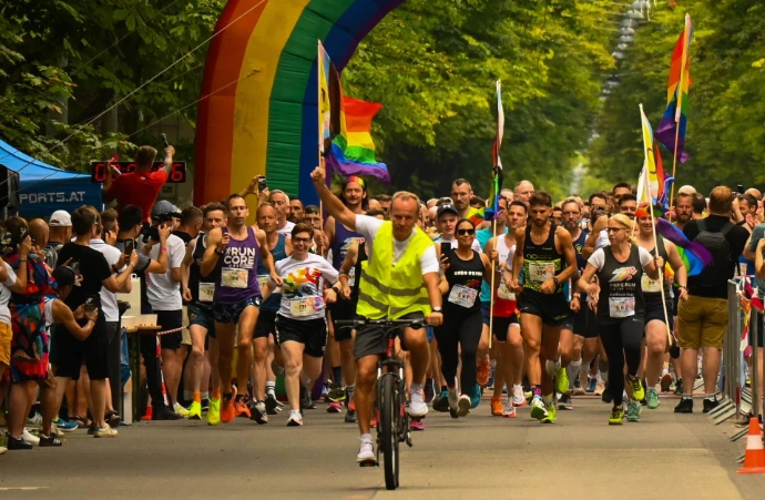 Big colorful group of people running under a rainbow gate and holding rainbow flags