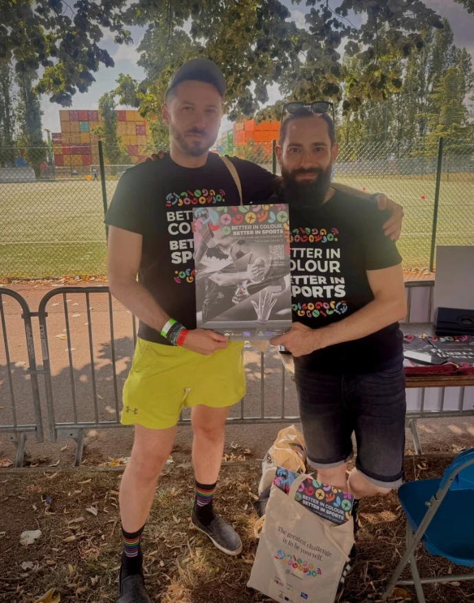Two smiling people holding a poster of Better in Colour, Better in Sports project